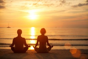 A couple sit on an idilic beach in a yogo pose. They are at peace and content. This is to illustrate the electrical engery of the body.